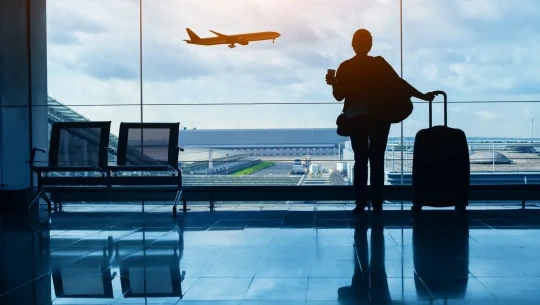 Woman with suitcase looking out window at an airplane mid flight