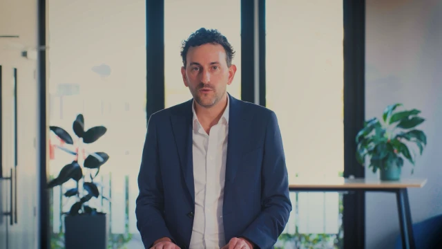 Man in suit standing in front of table with plants on it, in an office style setting