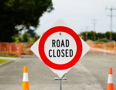 Red and white 'road closed' sign in the middle of a road, with orange road cones either side