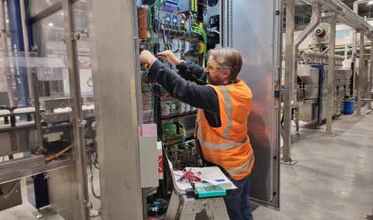 Man in high-vis clothing using tools to fix switchboard in factory