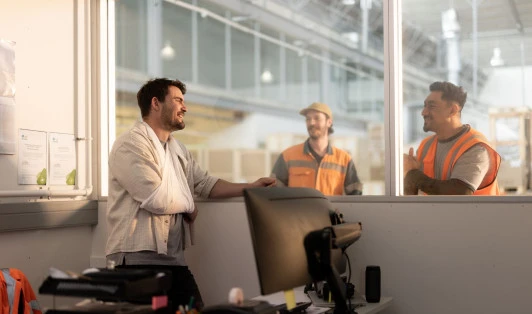 A man with his arm in a sling talks to two colleagues in high-vis gear