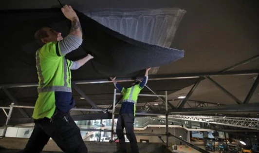 Two workers in high-vis clothing lifting a ceiling tile into place
