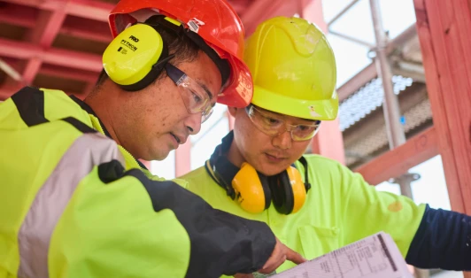 Two construction workers look at plans at a building site.