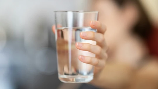 A hand holds a glass of water.