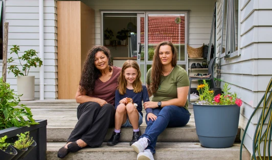 A grandmother, mother and daughter sit on a deck.