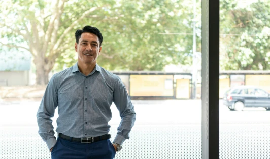Man stands with hands in pockets against a large window.