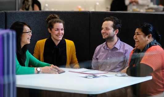 Four people sitting round a white table, smiling at each other.