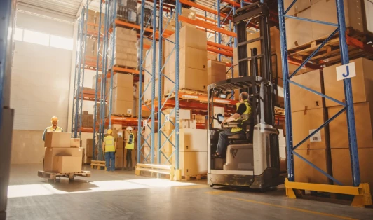 Workers drive forklifts inside a warehouse filled with boxes.