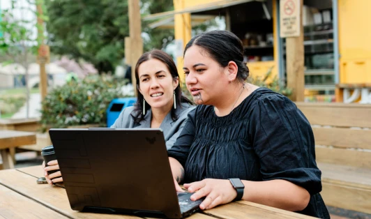 Two women sitting at a café table looking at a laptop.