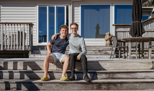 Two men sit on a deck of a house.