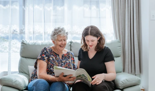 An older woman sits next to a younger woman on a sofa, looking at a tenancy agreement booklet.