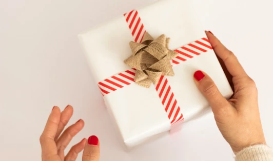 Two hands holding a gift wrapped in white paper with a red and white striped ribbon.