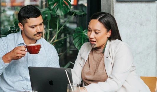 A woman looks at a laptop, next to a man holding a coffee cup.