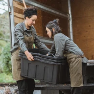 Two landscape gardeners lift equipment into a truck.